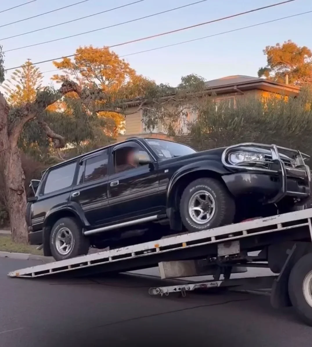 Black Toyota Land Cruiser 80 Series being driven off a tilt-tray truck on delivery